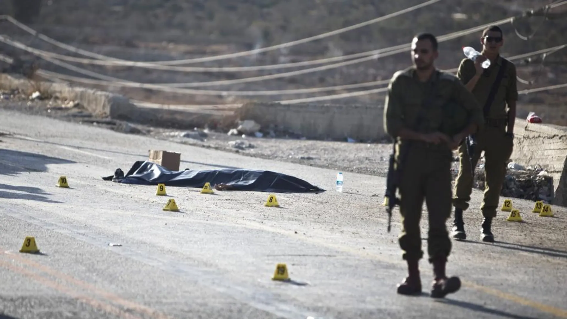 Dos soldados israelíes cusatodian el cadáver de un hombre en el lugar del ataque