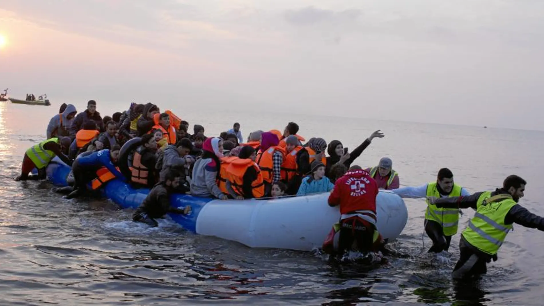 Un grupo de voluntarios ayuda a alcanzar la costa a un patera abarrotada de migrantes ayer en la isla griega de Lesbos