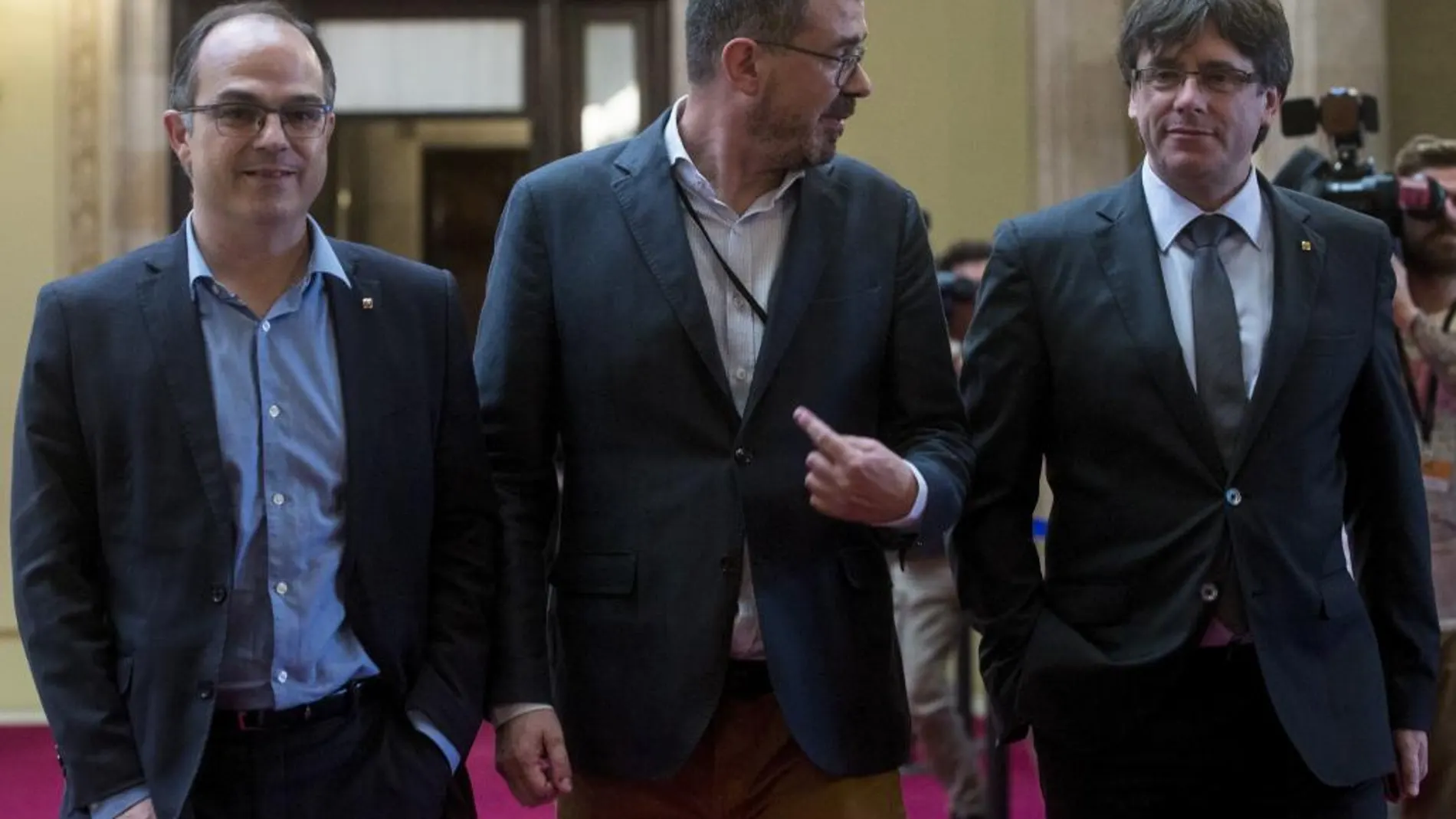 El presidente de la Generalitat de Cataluña, Carles Puigdemont, se dirige junto al director general de Comunicación de la Generalitat, Jaume Clotet, y el conseller de la Presidencia, Jordi Turull