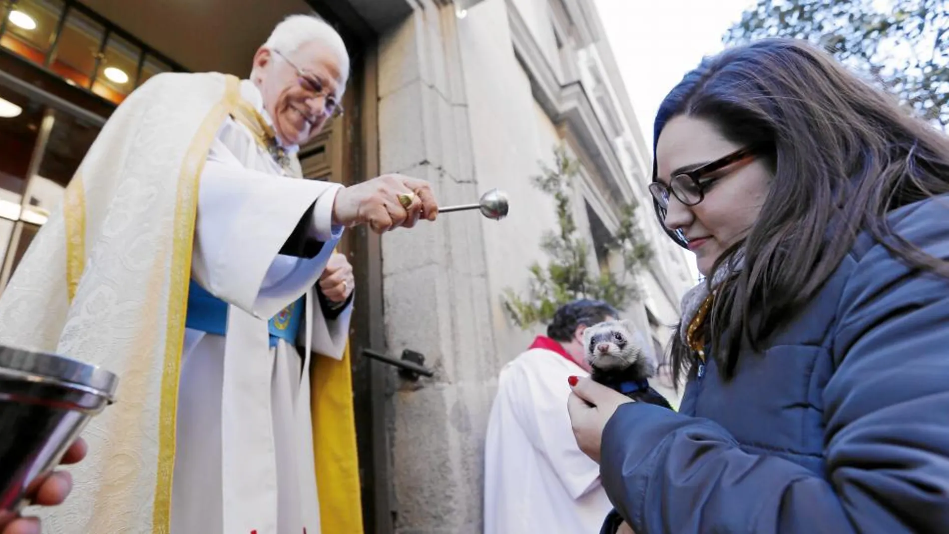 El padre Ángel bendice a un animal en la puerta de la iglesia de San Antón ante la atenta mirada de su dueña