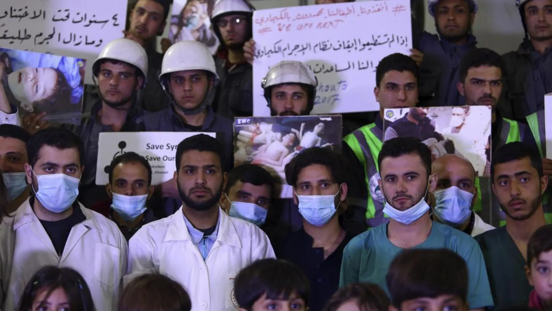 Voluntarios y personal de servicios de primeros auxilios sirios muestran pancartas e imágenes de las víctimas del ataque químico que se produo en jJan Shijún, durante una concentración para mostrar solidaridad con los fallecidos, en Douma (Siria)