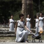 La actriz griega Katerina Lehú (d), en el papel de la Gran Sacerdotisa de Olimpia, enciende la llama mediante un espejo parabólico que desvía los rayos solares hacia la antorcha.