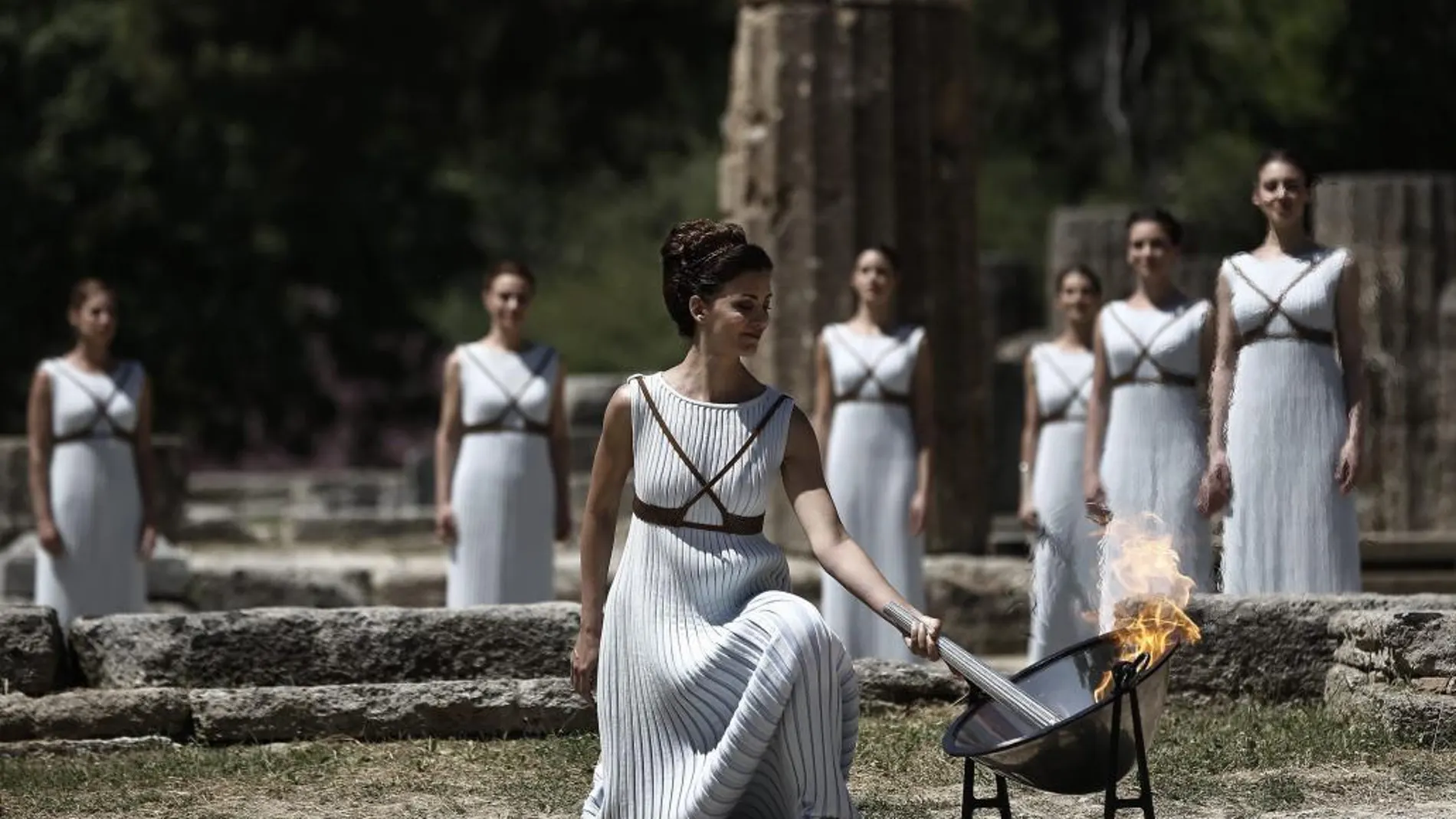 La actriz griega Katerina Lehú (d), en el papel de la Gran Sacerdotisa de Olimpia, enciende la llama mediante un espejo parabólico que desvía los rayos solares hacia la antorcha.