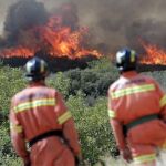 Dos bomberos observan las llamas cerca de la localidad de Sumacarcer, en el término valenciano de bolbaite