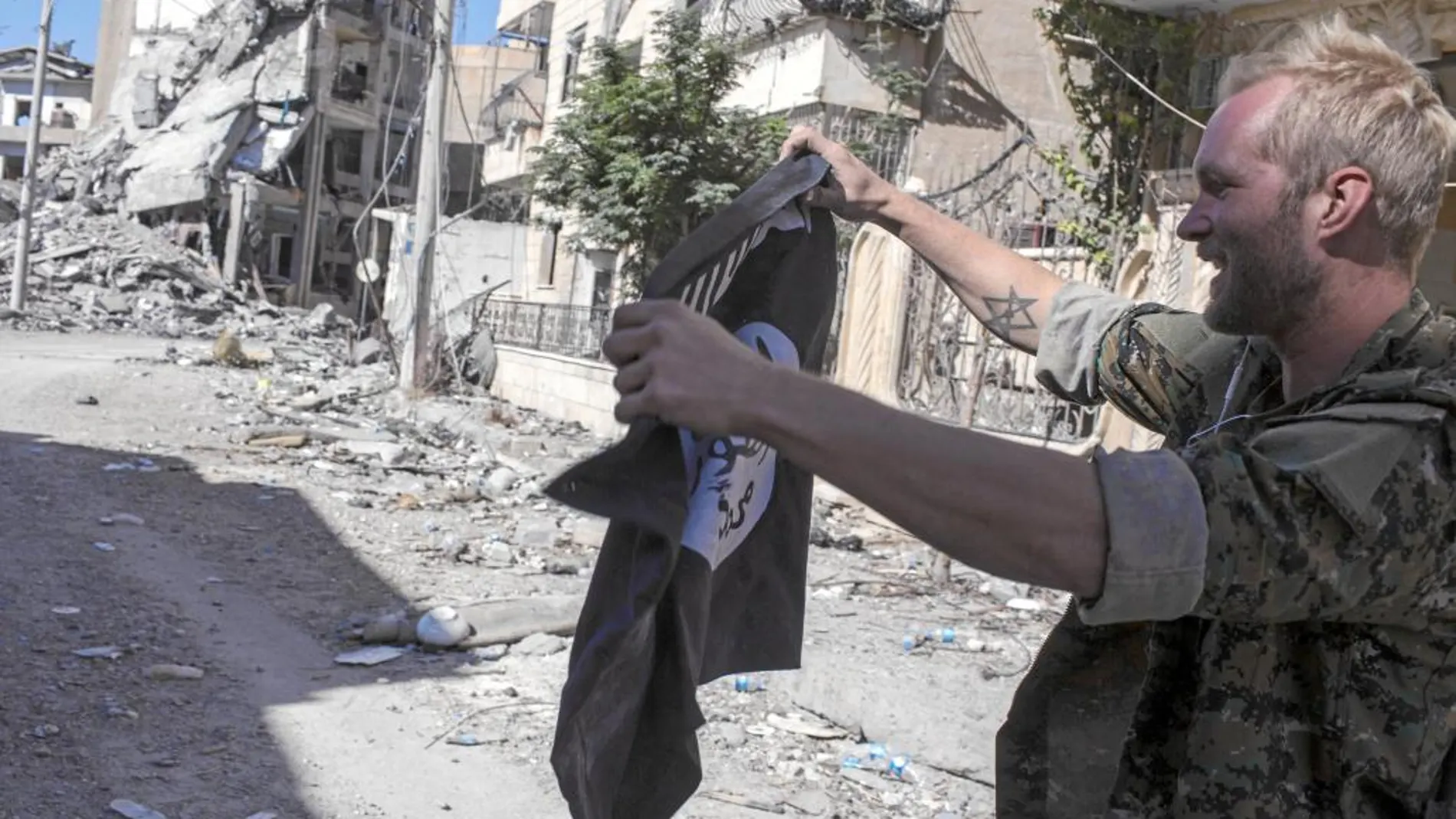 Un miliciano que participó en la derrota del EI en Raqa muestra una bandera yihadista