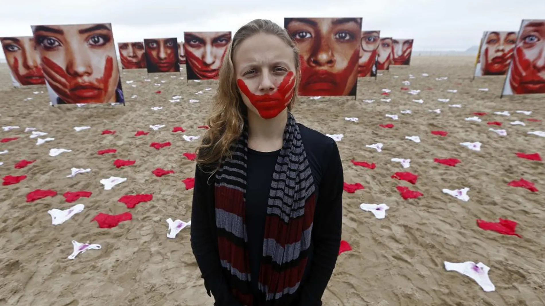 Imagen de 2016 de una voluntaria de la ONG Río de Paz posa en la playa de Copacabana junto a imágenes de modelos que representan a mujeres que sufrieron algún tipo de abuso sexual