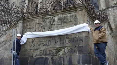Dos operarios colocan la lona para tapar la pintada "yo no salí de tu costilla, tú saliste de mi coño"