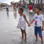 Dos niñas se dan la mano para ayudarse a su paso por una calle inundada en Les Cayes, Haití