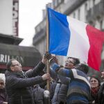 Varias personas colocan una bandera francesa frente a la cafetería le Carillon