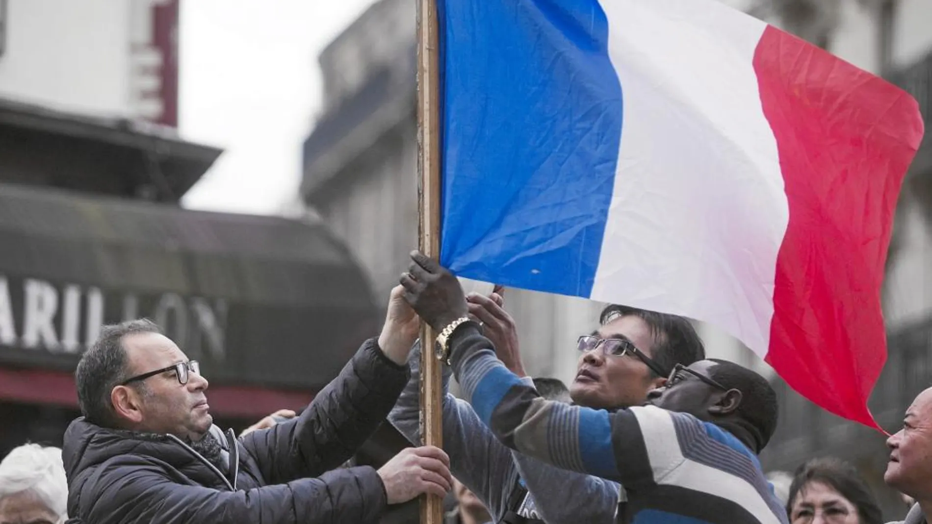 Varias personas colocan una bandera francesa frente a la cafetería le Carillon