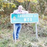 Jorge Val, alcalde de Alfoz, junto al cartel de la parroquía de Mor, que espera con impaciencia la declaración del humorista como conde