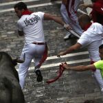 Varios mozos ante un toro de la ganadería de José Escolar Gil tras pasar la curva de Mercaderes durante el tercer encierro de los sanfermines 2016.