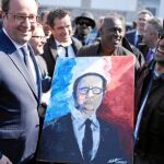 Un pintor local entrega, ayer, al presidente Hollande un retrato en un suburbio de París