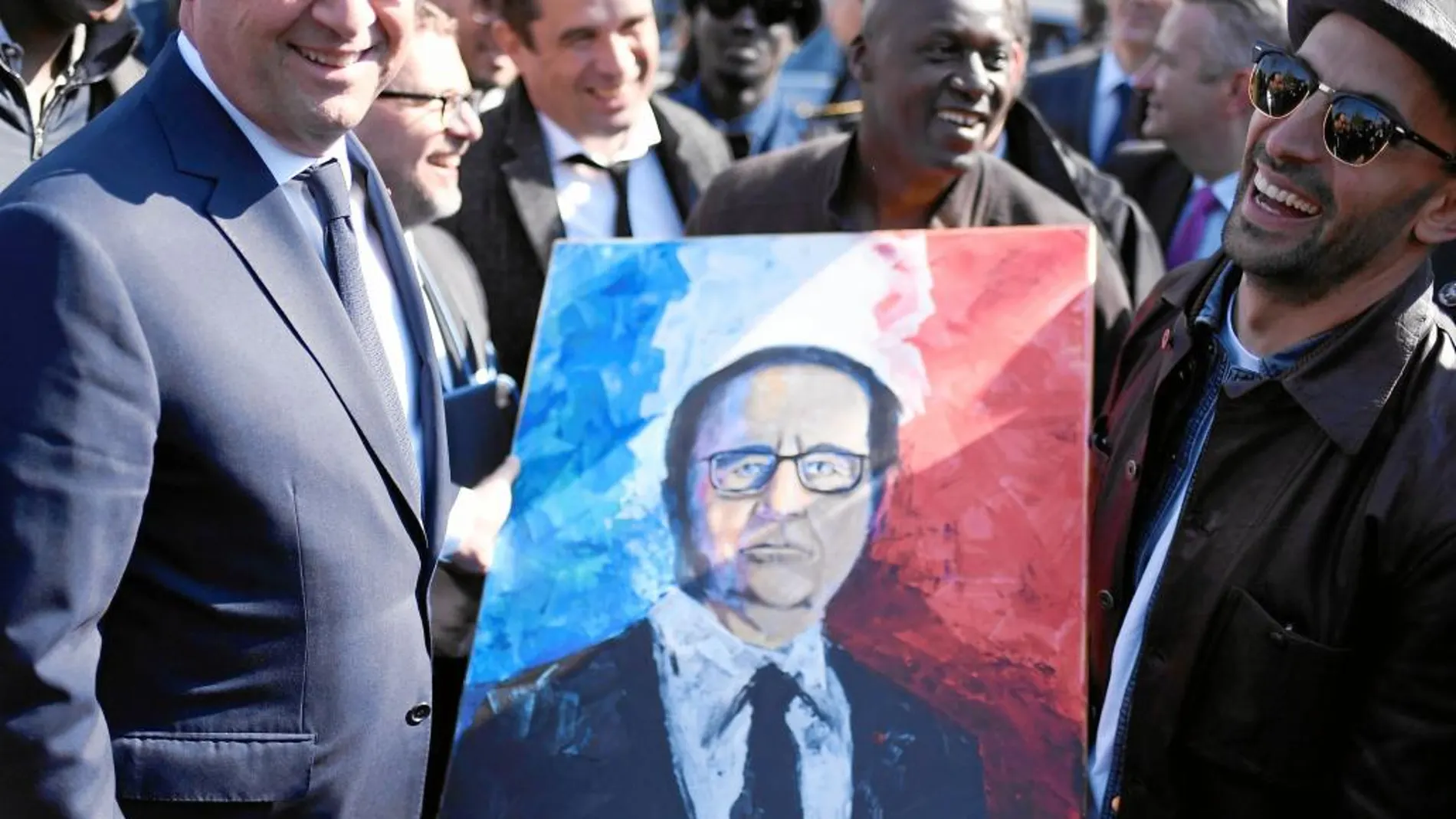 Un pintor local entrega, ayer, al presidente Hollande un retrato en un suburbio de París