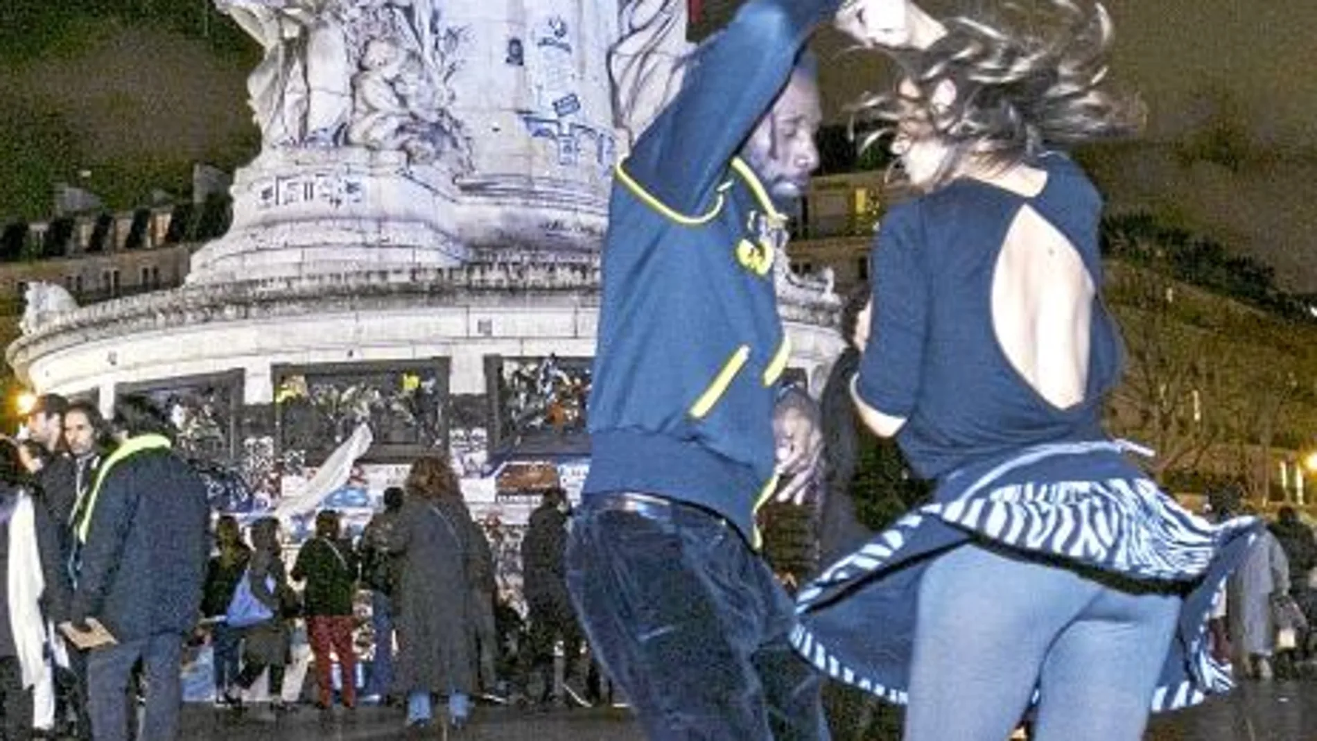 Dos jóvenes bailando frente a la plaza de la República de París, lugar donde los parisinos han rendido homenaje a las víctimas de los atentados del pasado viernes