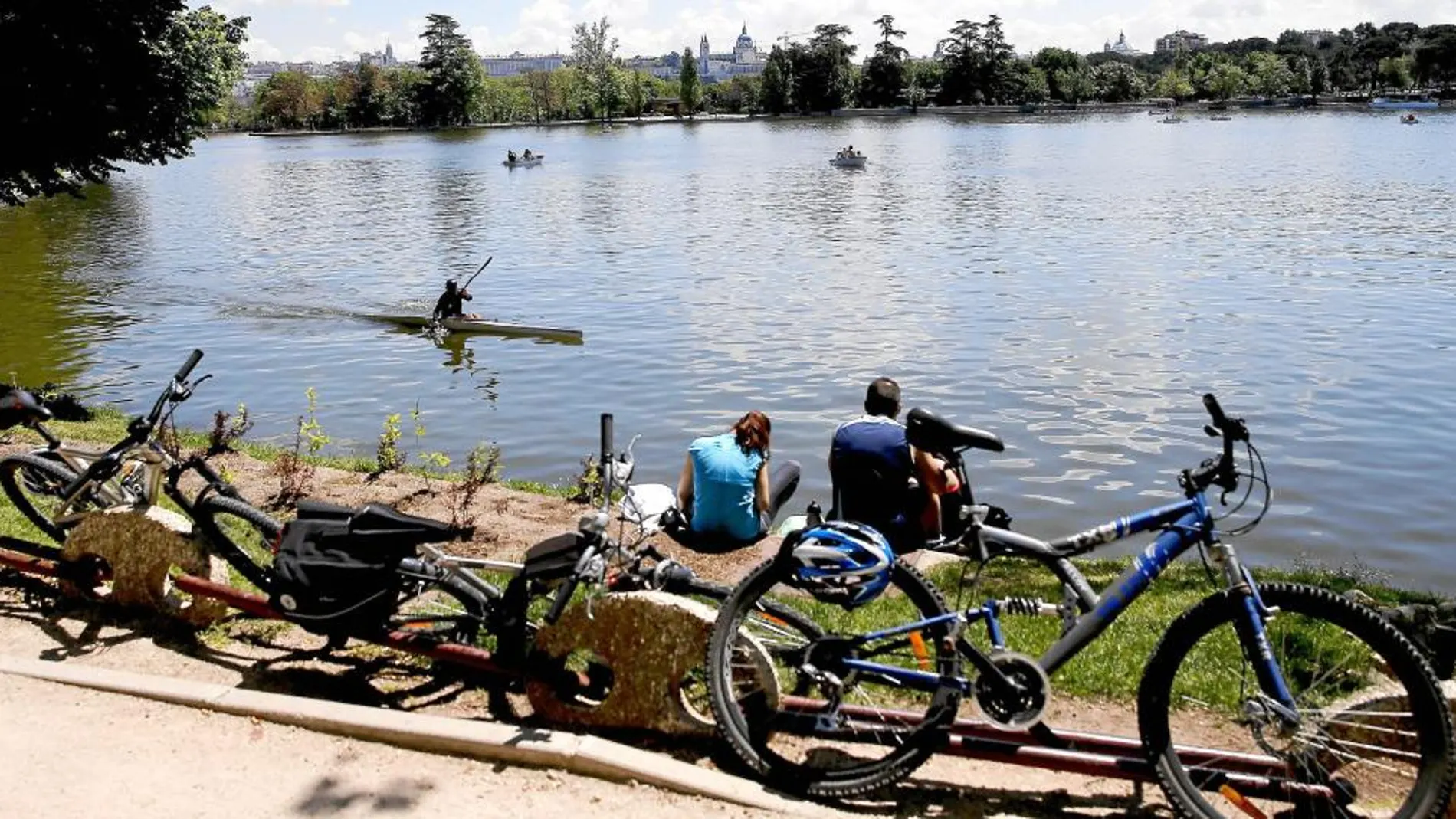 Varias personas junto a sus bicicletas descansan hoy junto al lago de la Casa de Campo de Madrid aprovechando las agradables temperaturas registradas en la capital.