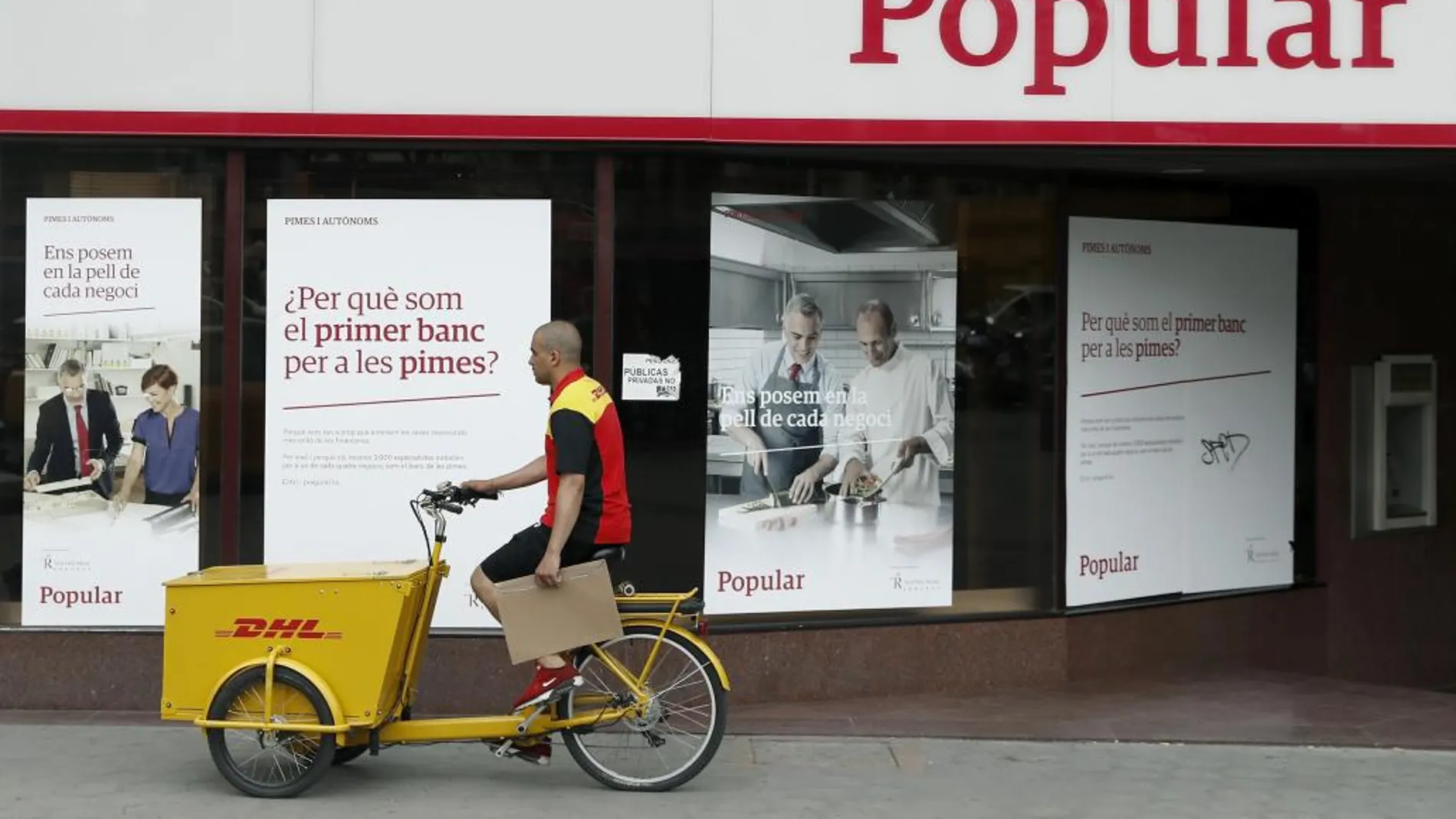 Un repartidor pasa ante una oficina del Banco Popular en el Paseo de Gracia esquina con la calle Aragón de Barcelona.