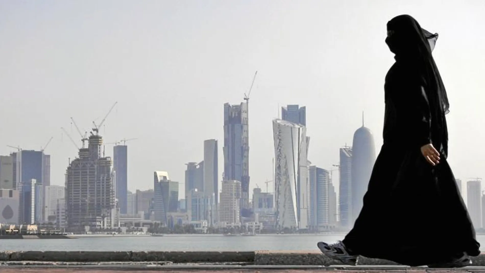Una mujer camina por el paseo marítimo con el perfil de Doha al fondo