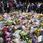 Varias personas contemplan las flores colocadas como homenaje a las víctimas del atentado terrorista d