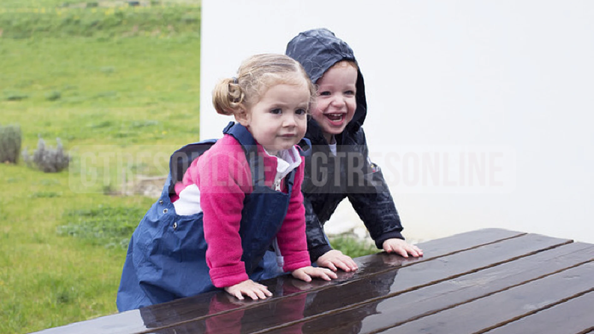 Un niño y una niña subidos sobre una mesa de madera mojada