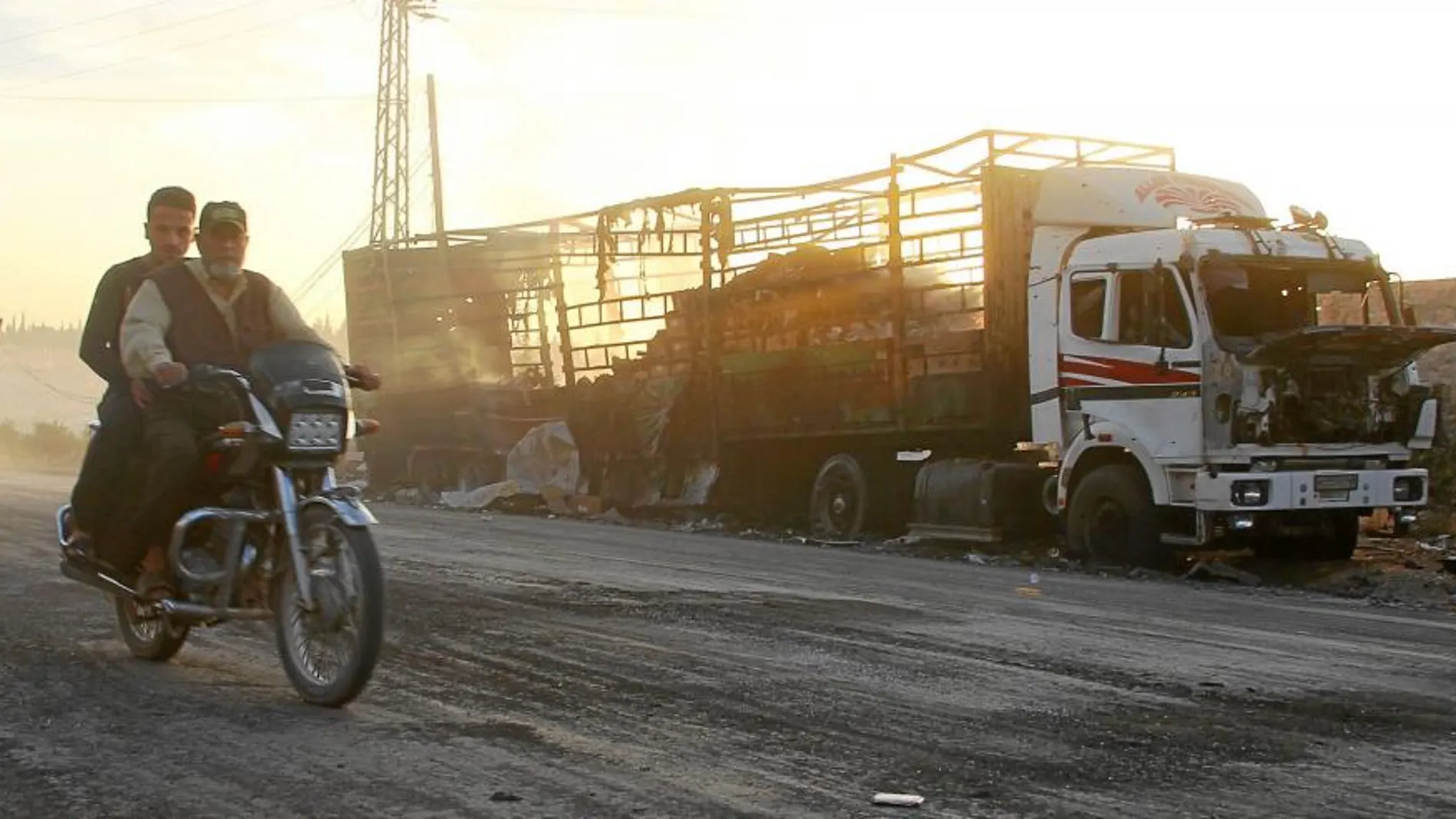 Una moto pasa frente a uno de los camiones de ayuda humanitaria que fueron calcinados cerca de Alepo