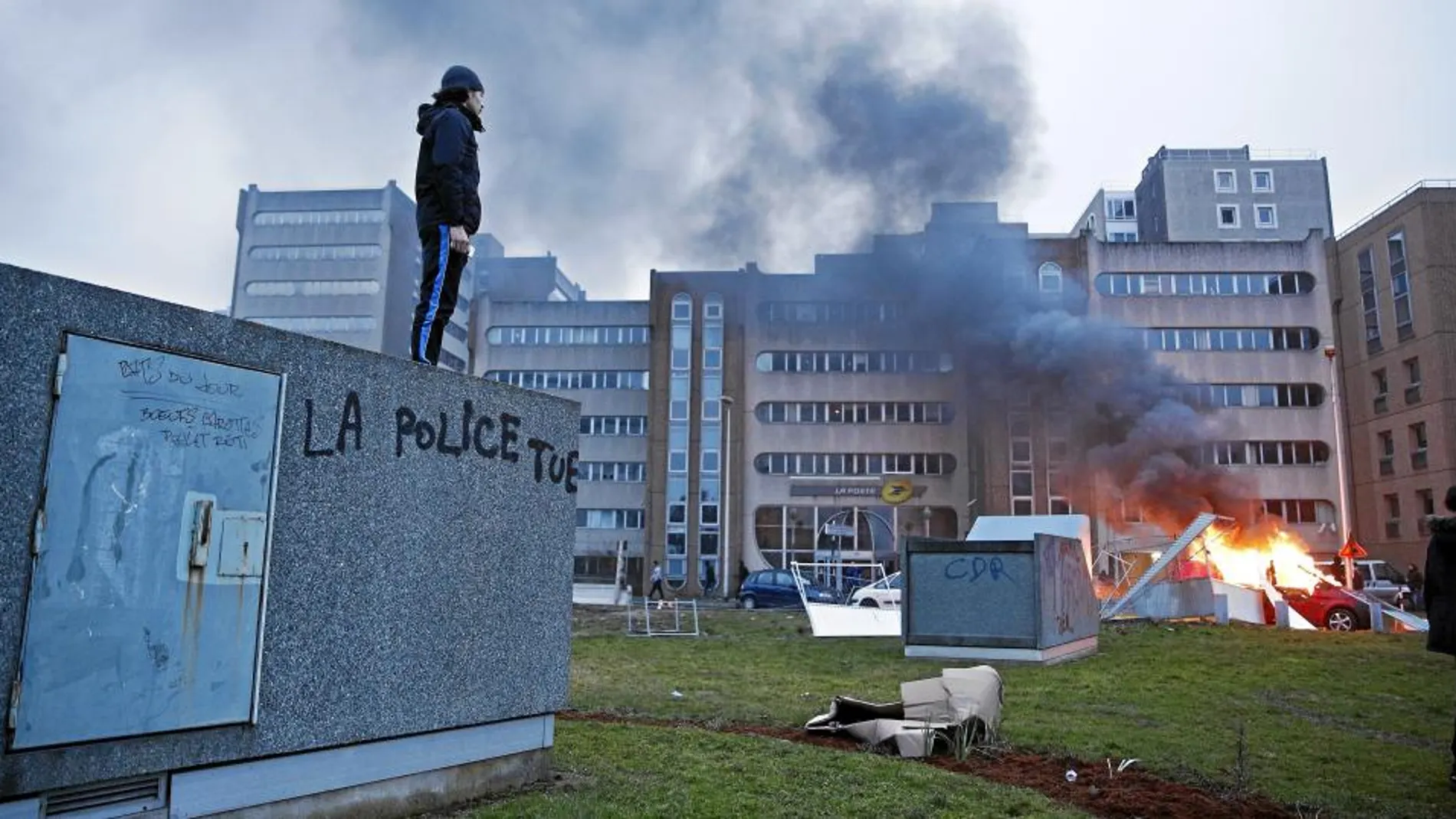 Un hombre observa un coche incendiado desde un muro donde se lee «La Policía mata», en el suburbio parisino de Bobigny