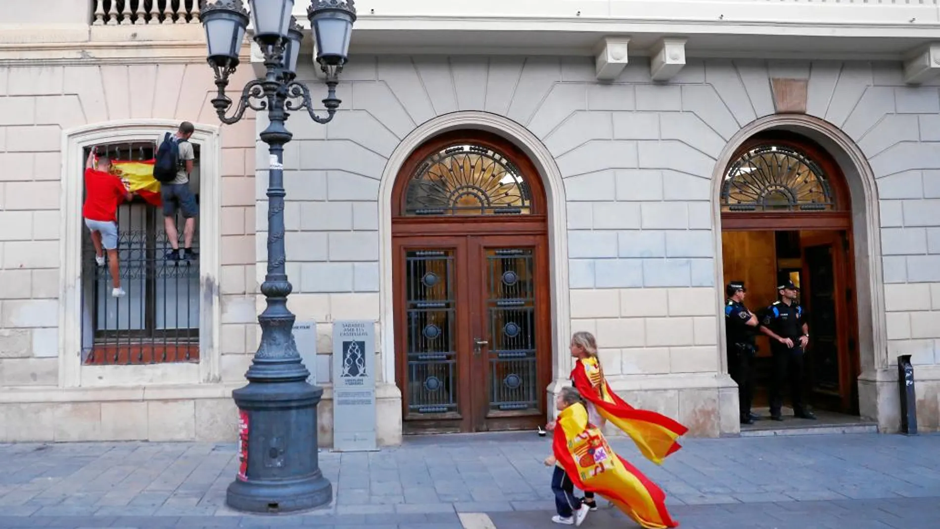 Dos niños pasean por el ayuntamiento de Sabadell con sendas banderas españolas, ayer, mientras dos personas cuelgan la misma insignia en una ventana