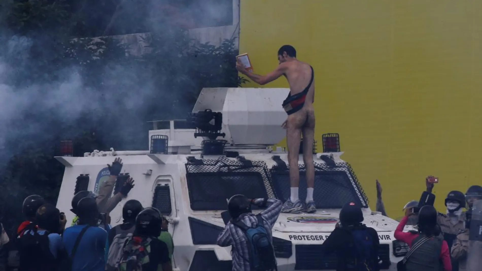 Un hombre desnudo permanece subido a un vehículo de la Guardina Nacional Bolivariana hoy en Caracas.