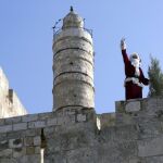 Issa, un joven palestino disfrazado de Papá Noel, saluda a los viandantes desde lo alto de la muralla de ciudad vieja de Jerusalén (Israel)