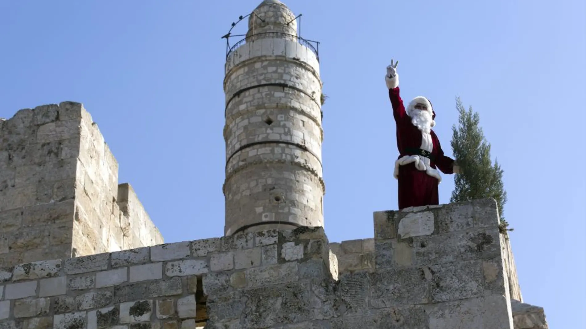 Issa, un joven palestino disfrazado de Papá Noel, saluda a los viandantes desde lo alto de la muralla de ciudad vieja de Jerusalén (Israel)