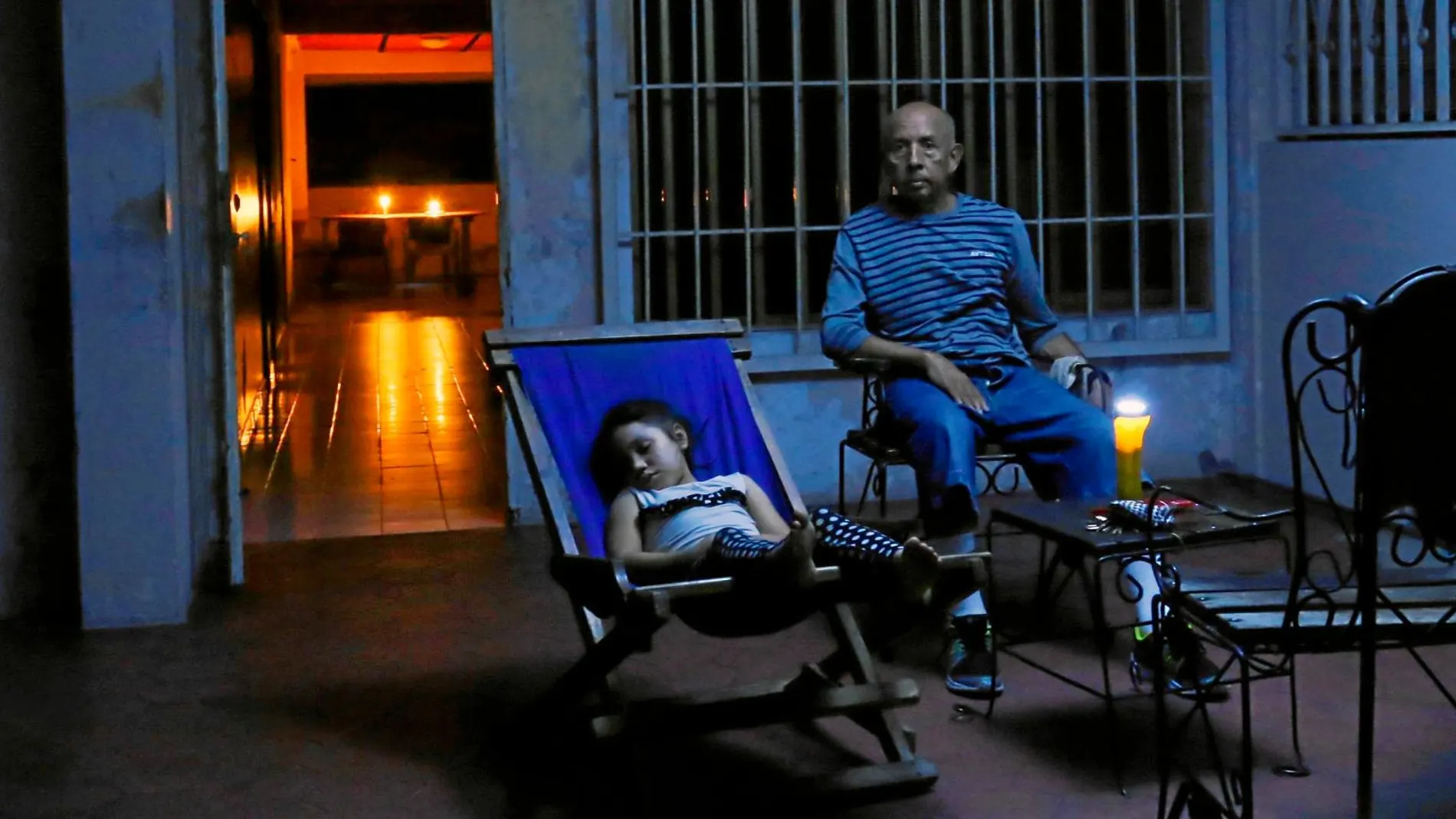 Un hombre y un niño sentados en un patio en una casa de Caracas alumbrados con velas ante la falta de suministro eléctrico / Reuters