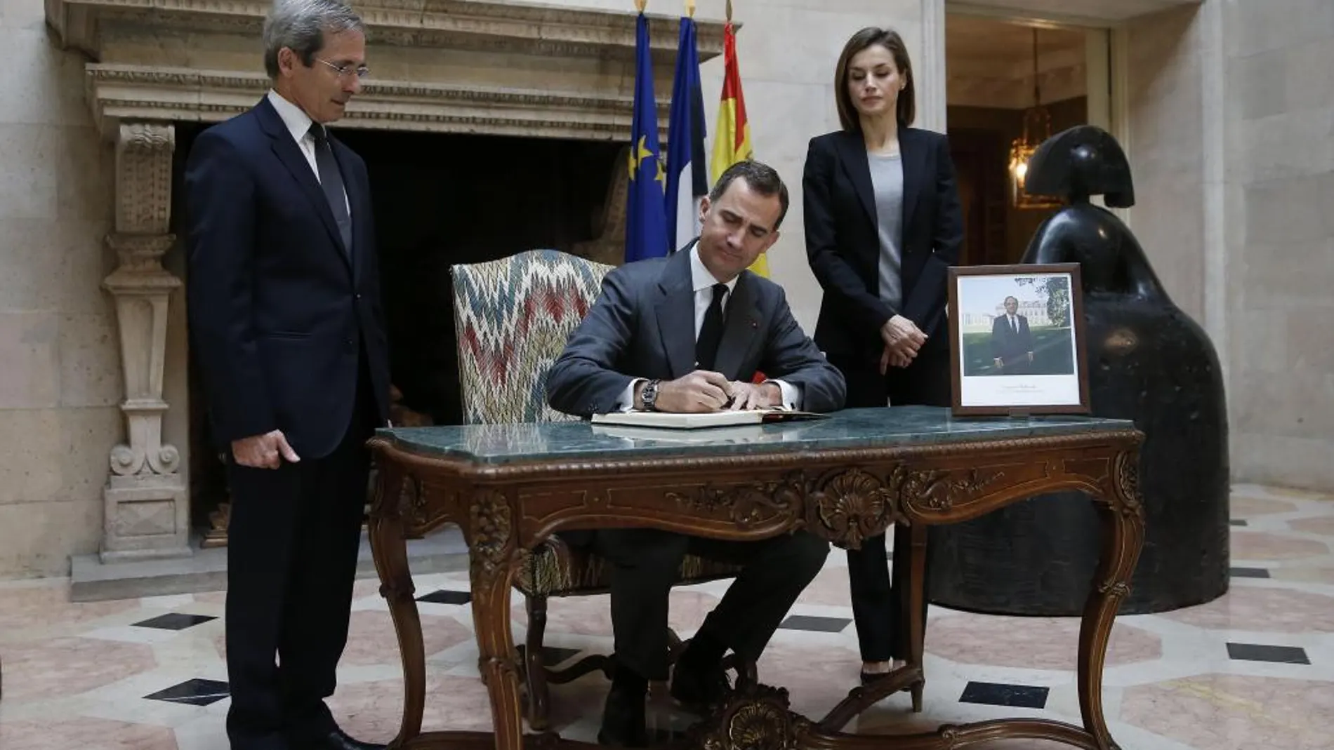 El Rey Felipe VI, junto a la Reina Letizia y el embajador de Francia en España, Yves Saint-Geours (i), firma en el libro de condolencias instalado en el vestíbulo de la residencia del embajador francés en Madrid por los atentados terroristas de ayer en París.