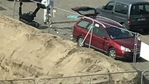 Un artificiero con un robot de desactivación de explosivos junto al coche del sospechoso