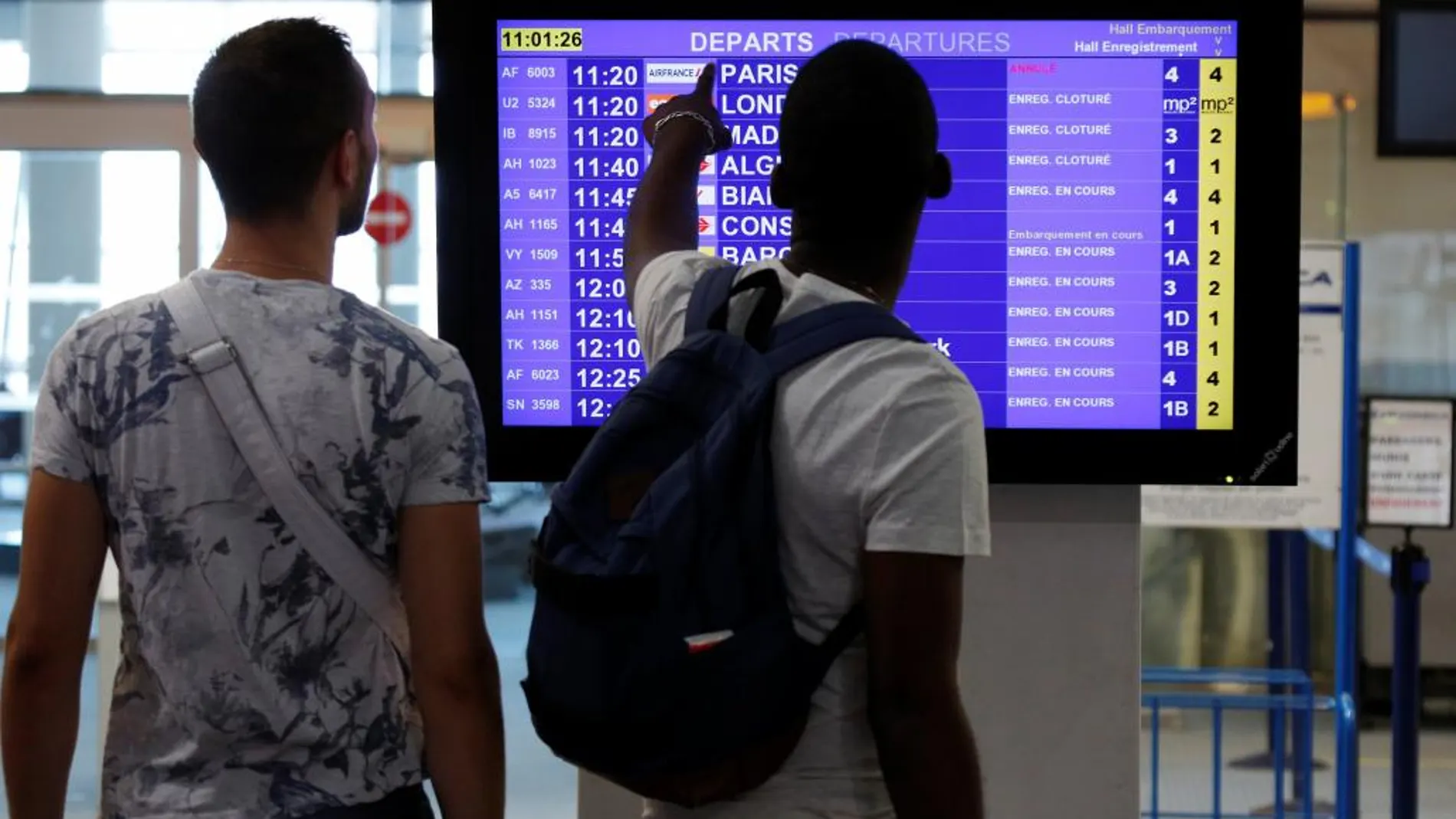 Unos pasajeros comprueban la anulación de un vuelo de Air France en un panel informativo.
