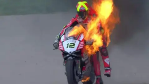 Xavi Forés sujetando su moto en llamas