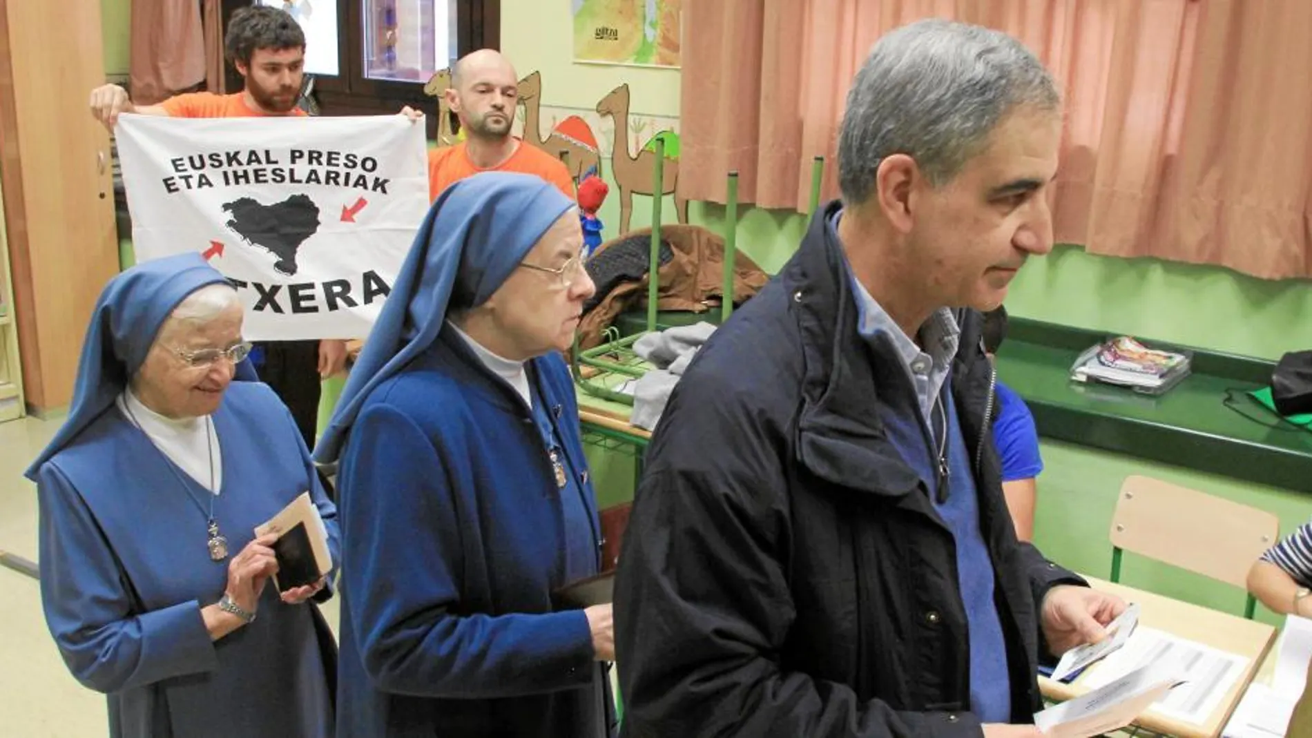 Leopoldo Barrera, cabeza del PP por Vizcaya, al ir a votar, mientras apoderados de Bildu muestran una bandera a favor del acercamiento de presos de ETA