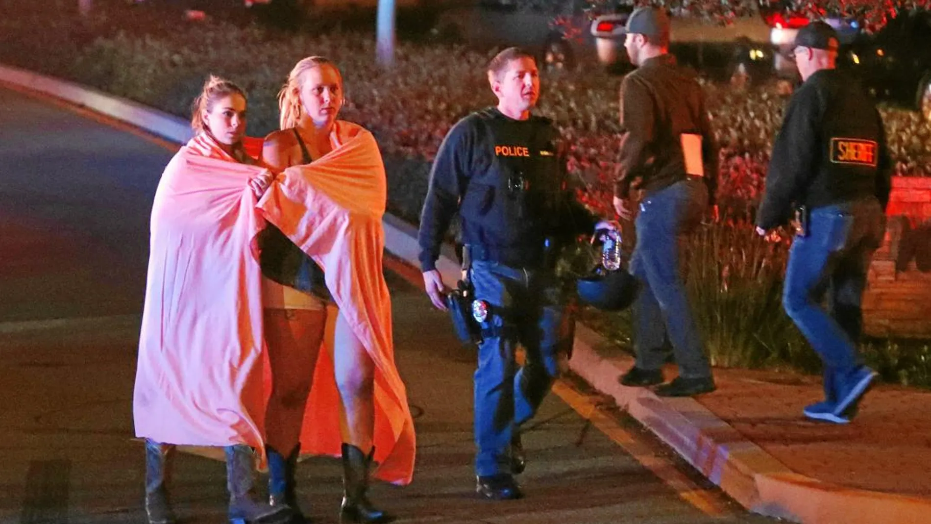 Dos mujeres envueltas en una manta abandonan el área del bar donde se produjo el tiroteo