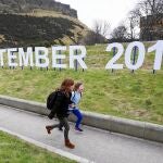 Dos niñas caminan delante de un cartel con la fecha del próximo referéndum escocés, frente al Parlamento de Edimburgo