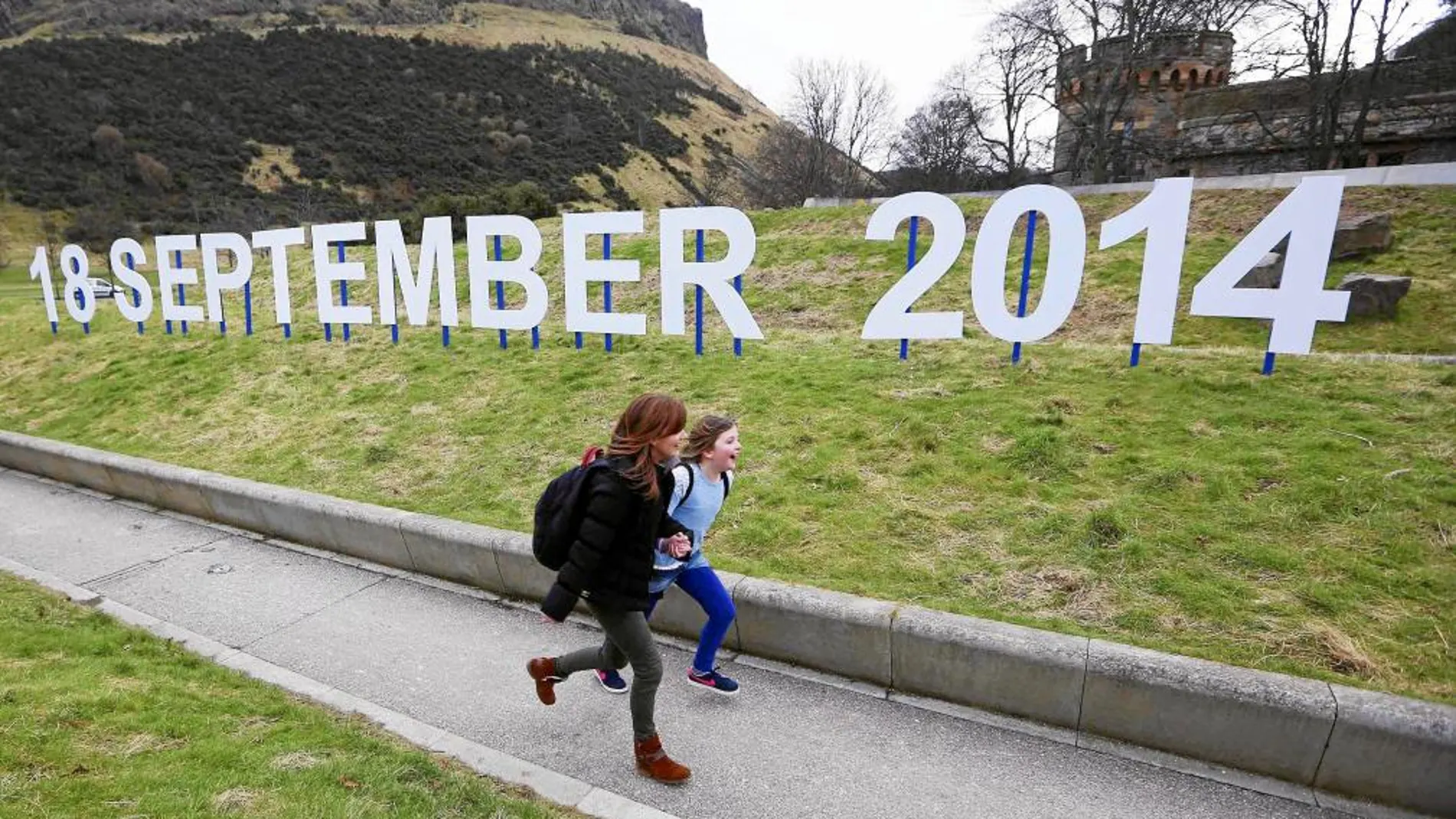 Dos niñas caminan delante de un cartel con la fecha del próximo referéndum escocés, frente al Parlamento de Edimburgo