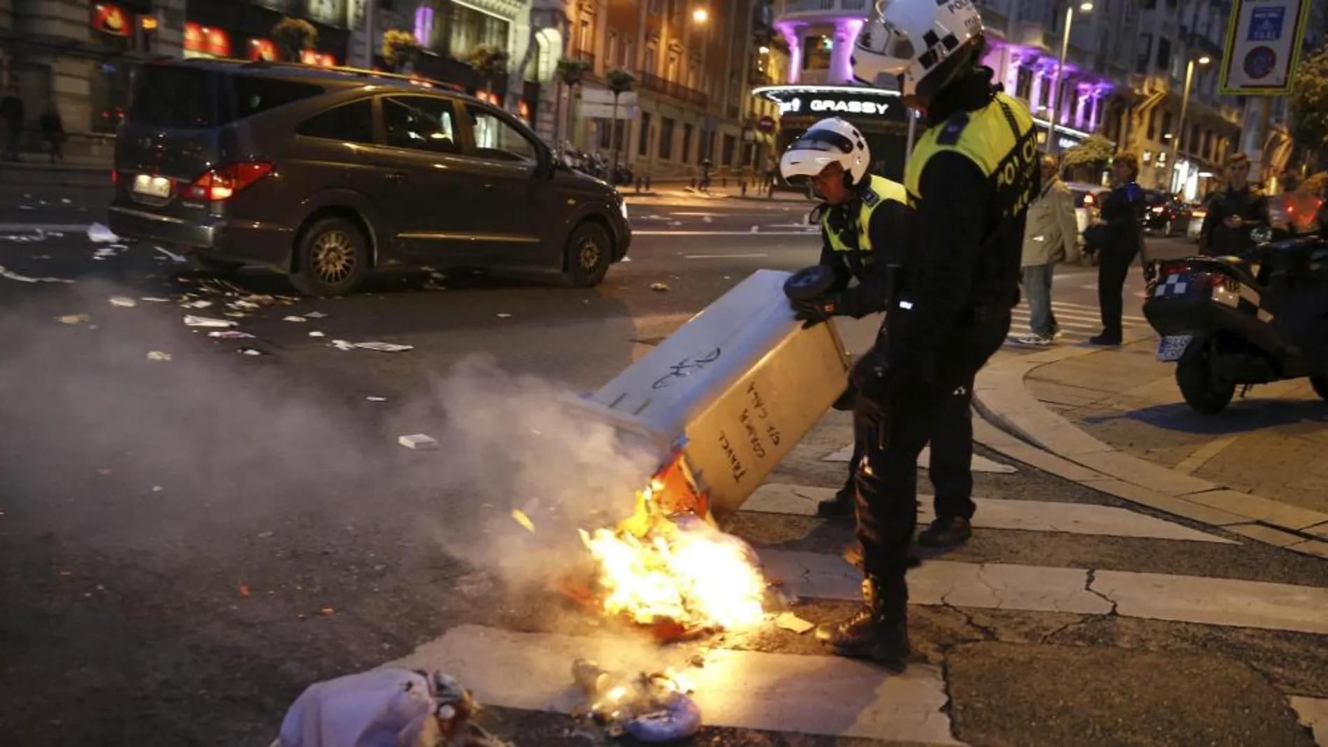 Policías municipales intentan apagar un contenedor incendiado en la calle Alcalá, junto a la Plaza de Cibeles