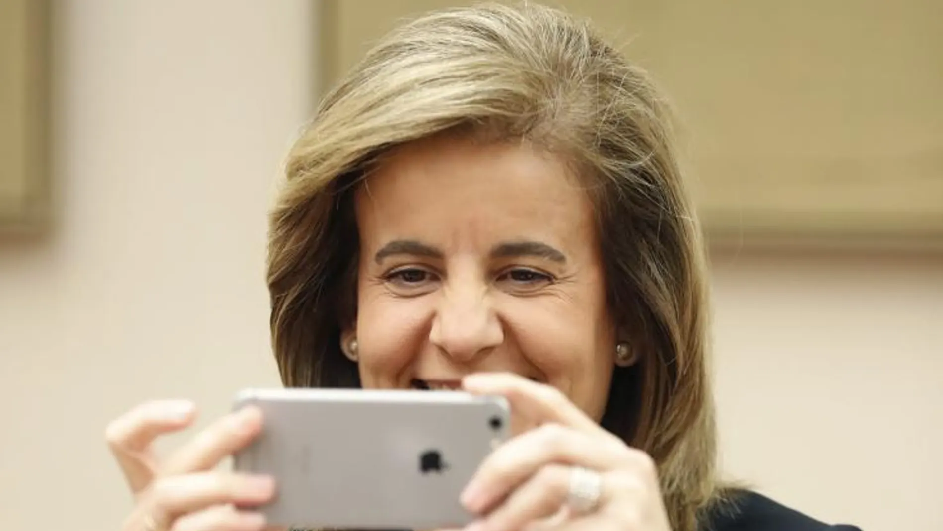 La ministra de Empleo, Fátima Báñez, hace una foto con su teléfono móvil a los fotógrafos, antes de su comparecencia en la Comisión de Empleo y Seguridad Social