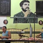 Dos cubanos trabajan en la carnicería de un mercado de La Habana de cuya pared cuelga un retrato del Che