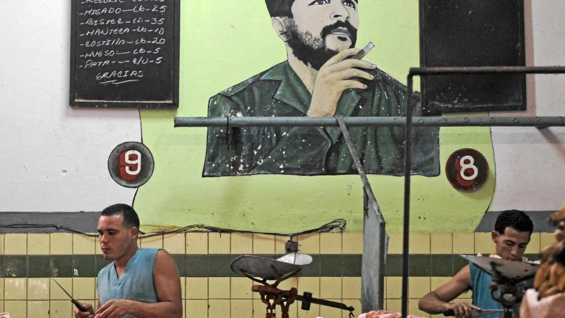 Dos cubanos trabajan en la carnicería de un mercado de La Habana de cuya pared cuelga un retrato del Che