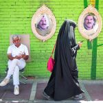Una mujer vestida con niqab camina por Teherán con carteles electorales rasgados de fondo