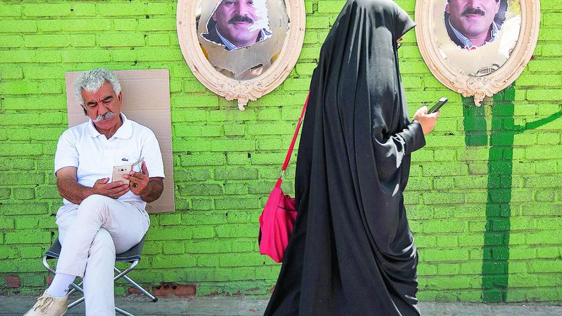 Una mujer vestida con niqab camina por Teherán con carteles electorales rasgados de fondo