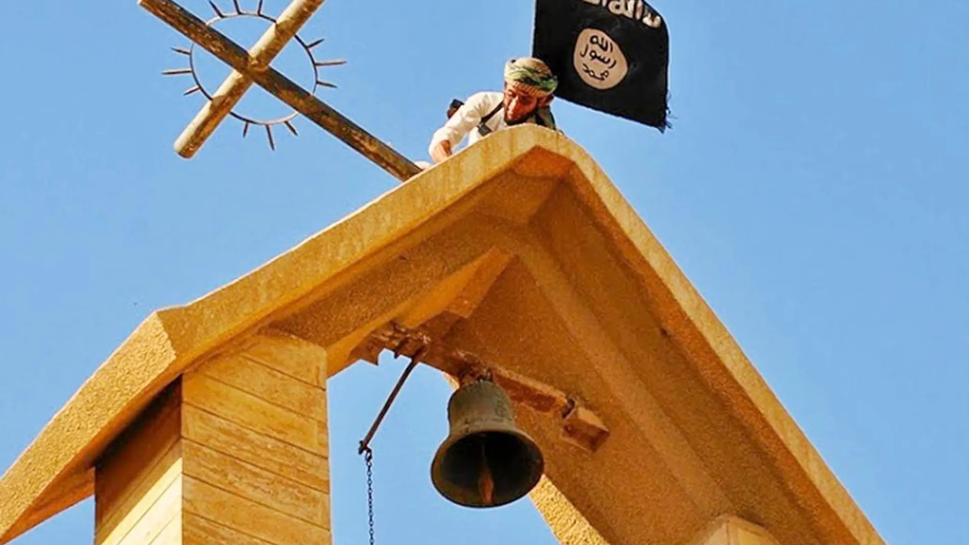Un miembro del EI sujeta la bandera mientras derriba una cruz en Mosul