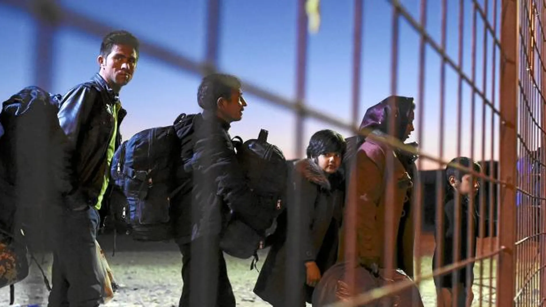 Varios refugiados cargan con sus pertenencias tras abandonar el campo de refugiados de Gevgelija, Macedonia, camino a la estación de autobuses para dirigirse a Serbia