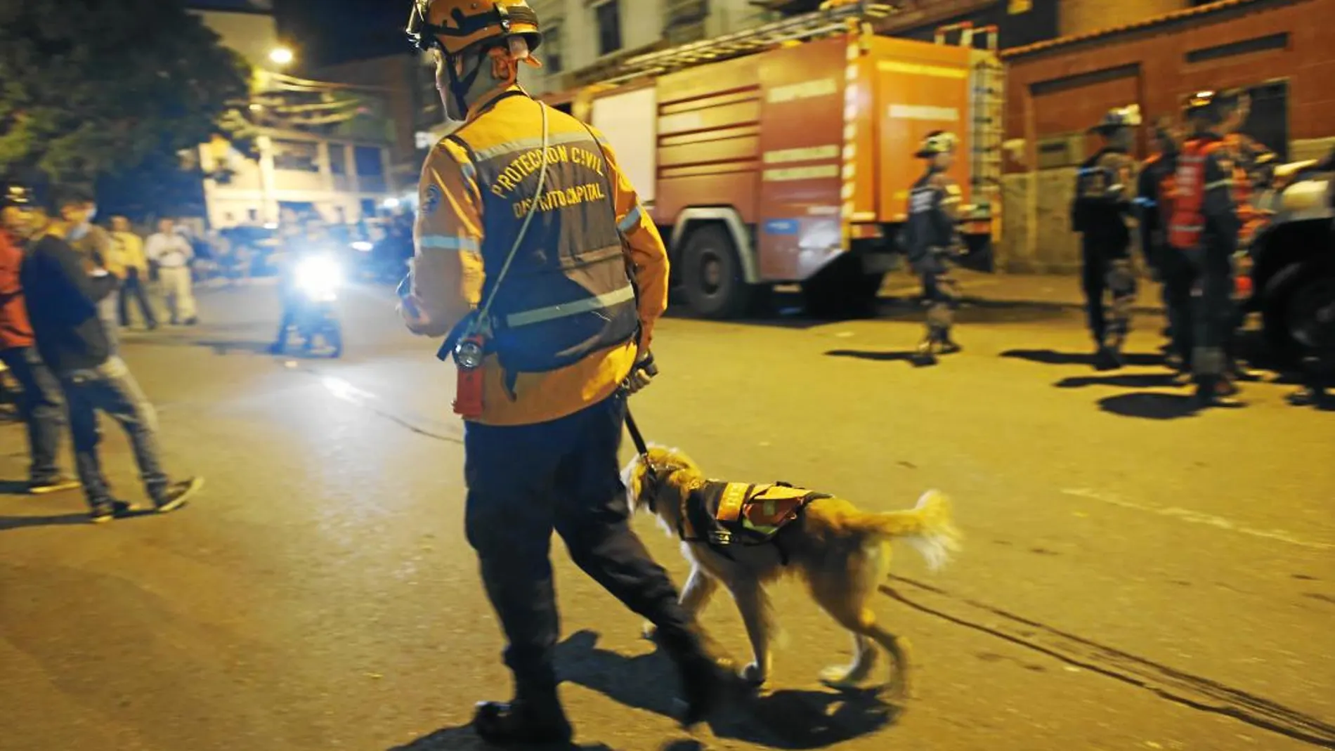 Un agente de Protección Civil, acompañado de su perro, comprueba los desperfectos en Caracas tras el seísmo
