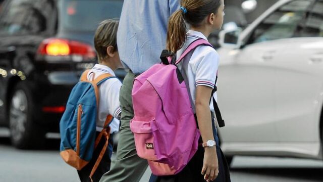 En la imagen, un padre acompañando a sus dos hijos a la escuela