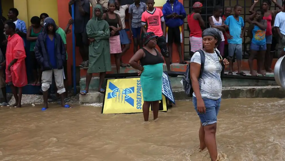 Personas intentan cruzar una calle inundada tras el paso del huracán Matthew en Leogane (Haití)